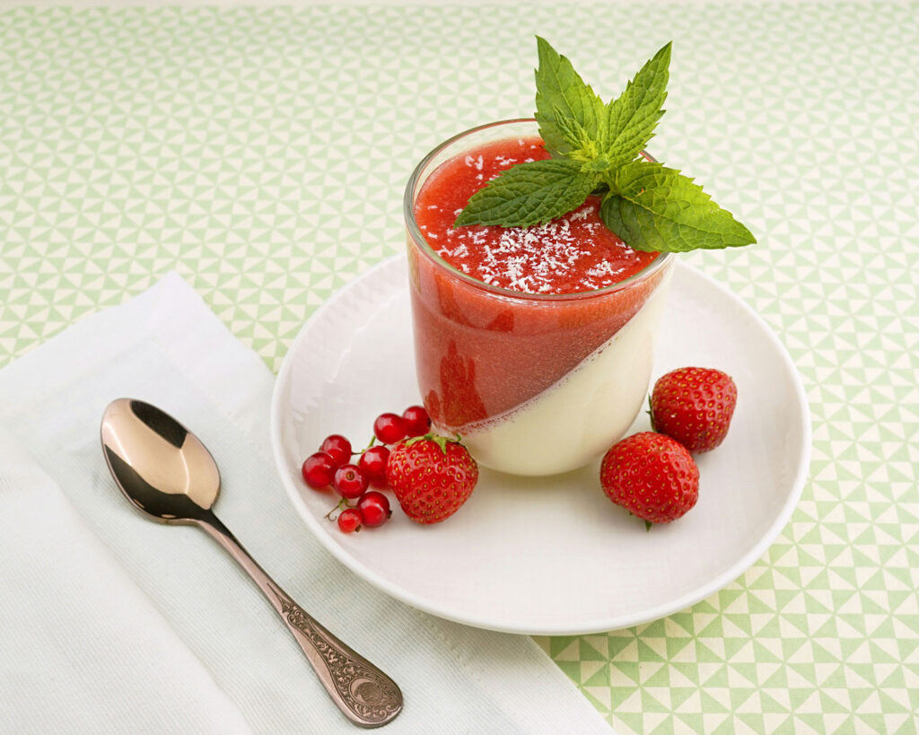 Panna Cotta im Glas mit Erdbeerspiegel, frischen Beeren und Minzblatt – sommerlich-frisches Dessert aus Italien.