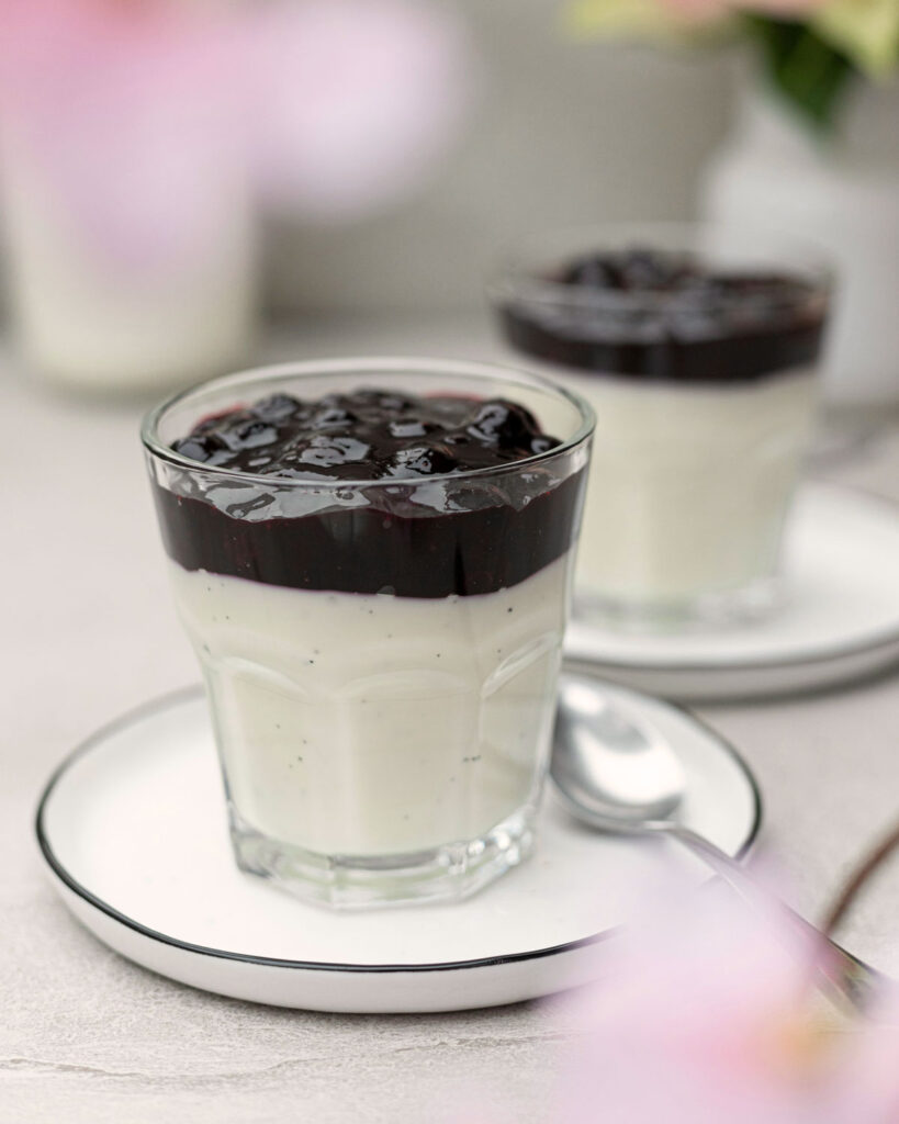 Panna Cotta mit dunkler Waldfrucht-Kompott im Glas serviert – cremig, fruchtig und typisch italienisch.
