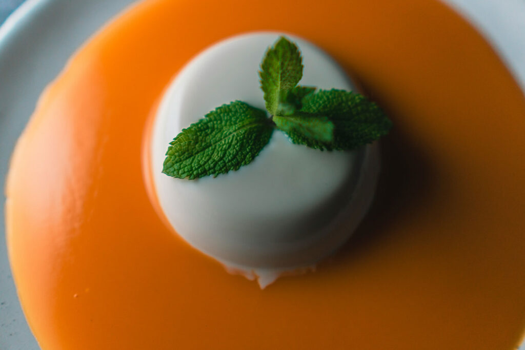 Nahaufnahme einer klassischen Panna Cotta mit Mangosauce und Minzblatt – perfekte Kombination aus Süße und Frische.
