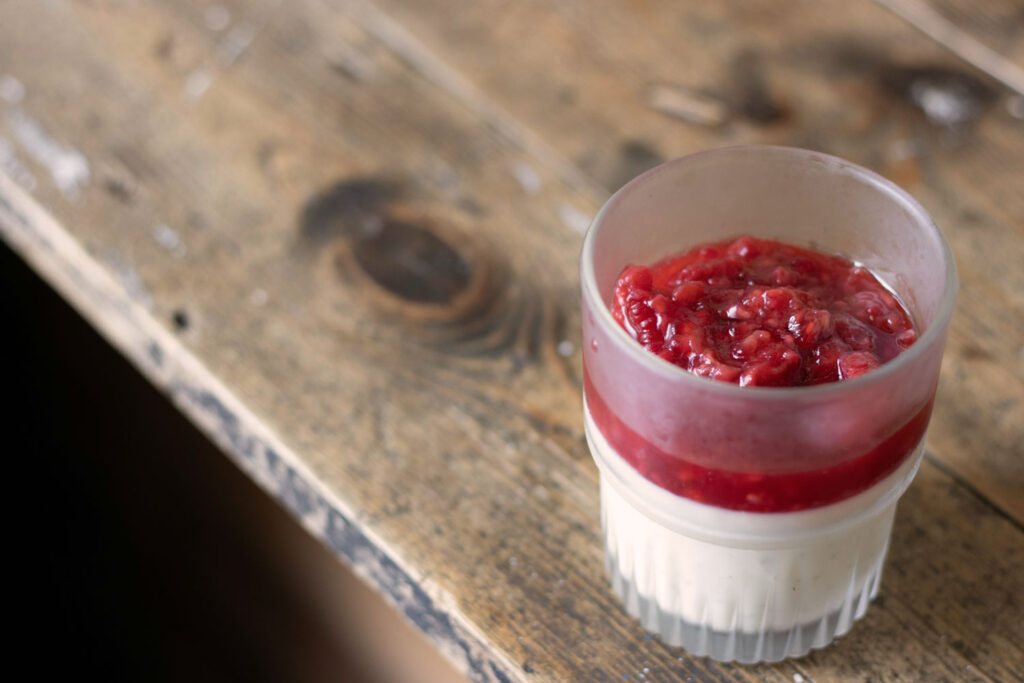 Rustikale Panna Cotta mit Himbeerspiegel im Vintage-Glas – serviert auf einem alten Holztisch für authentische Atmosphäre.