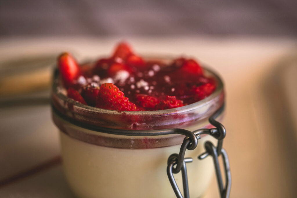 Hausgemachte Panna Cotta im Einmachglas, garniert mit Erdbeeren und fruchtiger Beerensauce.