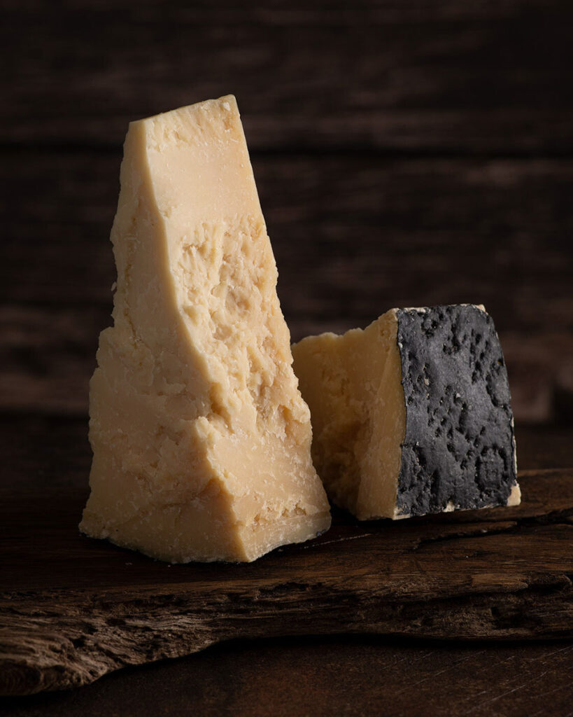 Zwei Stücke Pecorino Romano auf rustikalem Holzbrett, einer mit schwarzer Wachsrinde – gereifter Schafskäse mit körniger Textur, Symbol für italienische Käsetradition.