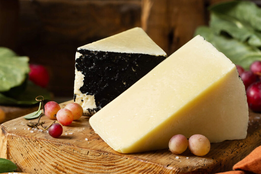 Zwei Stücke Pecorino Romano, einer mit schwarzer Rinde, angerichtet mit Weintrauben auf einem Holzbrett – mediterrane Ästhetik trifft auf kräftige Aromen.