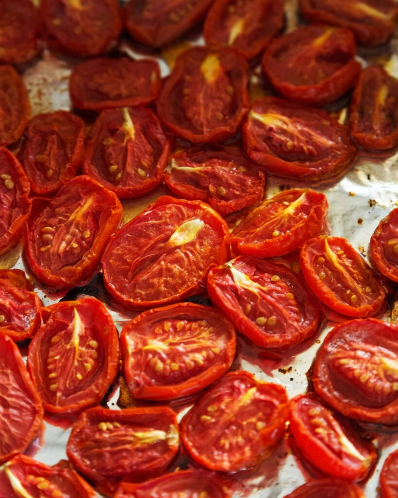 Nahaufnahme halbgetrockneter Tomaten auf Backpapier, frisch aus dem Ofen – intensiv rot, saftig und aromatisch.