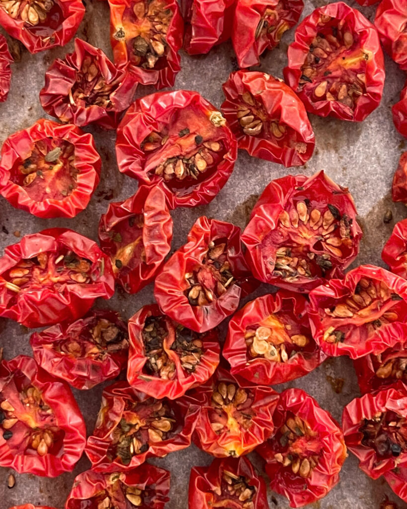 Ofengetrocknete Cherrytomaten mit Kräutern, eng aneinandergereiht auf Backpapier – leuchtend rot und würzig.