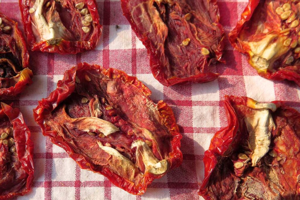 Getrocknete Tomatenhälften vom Typ San Marzano auf einem karierten Küchentuch – ein traditioneller Anblick aus Süditalien während der Sommertrocknung in der Sonne.