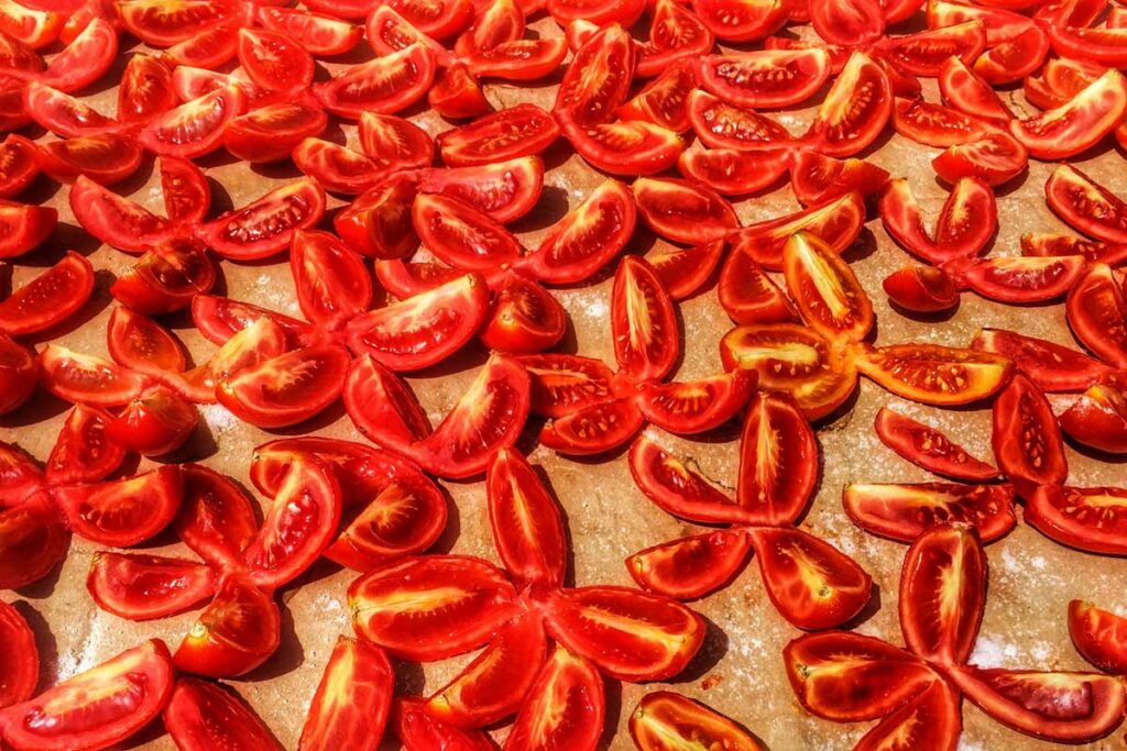 Aufgeschnittene Roma-Tomaten in Sternform, ausgebreitet unter südlicher Sonne – der erste Schritt zur traditionellen Herstellung von Pomodori Secchi.