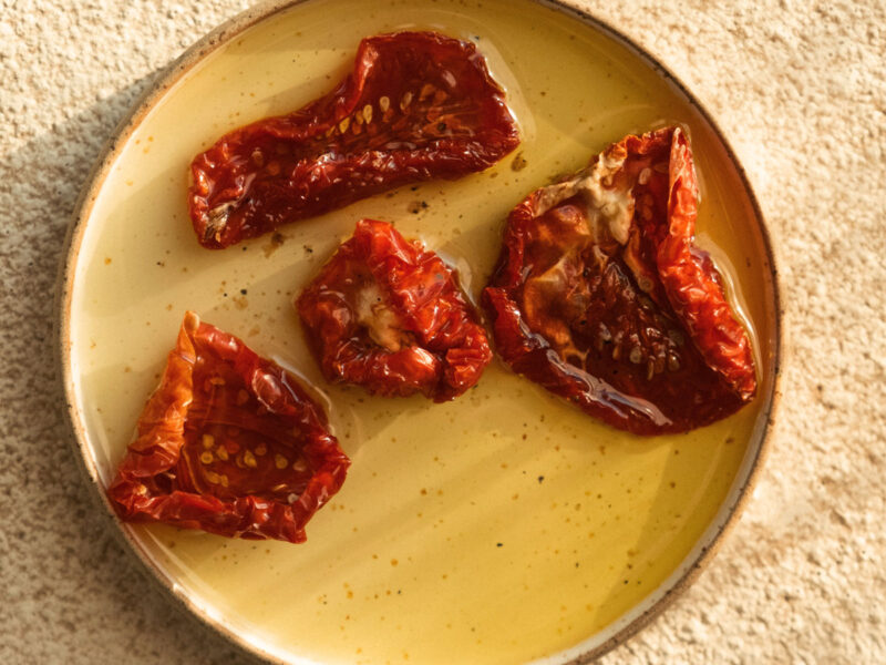Detailansicht eingelegter getrockneter Tomaten auf Olivenöl, serviert auf einem runden Keramikteller in warmem Sonnenlicht.
