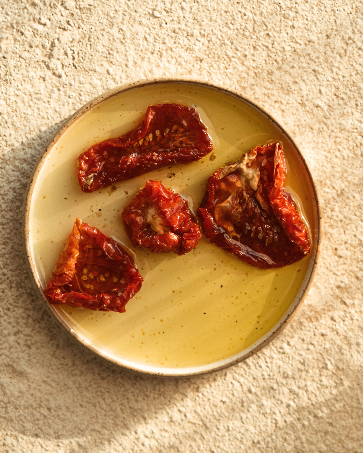 Detailansicht eingelegter getrockneter Tomaten auf Olivenöl, serviert auf einem runden Keramikteller in warmem Sonnenlicht.