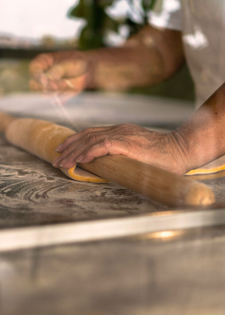 Traditionelle italienische Handarbeit: Ein Nudelholz rollt frischen Pastateig auf einem bemehlten Tisch aus.