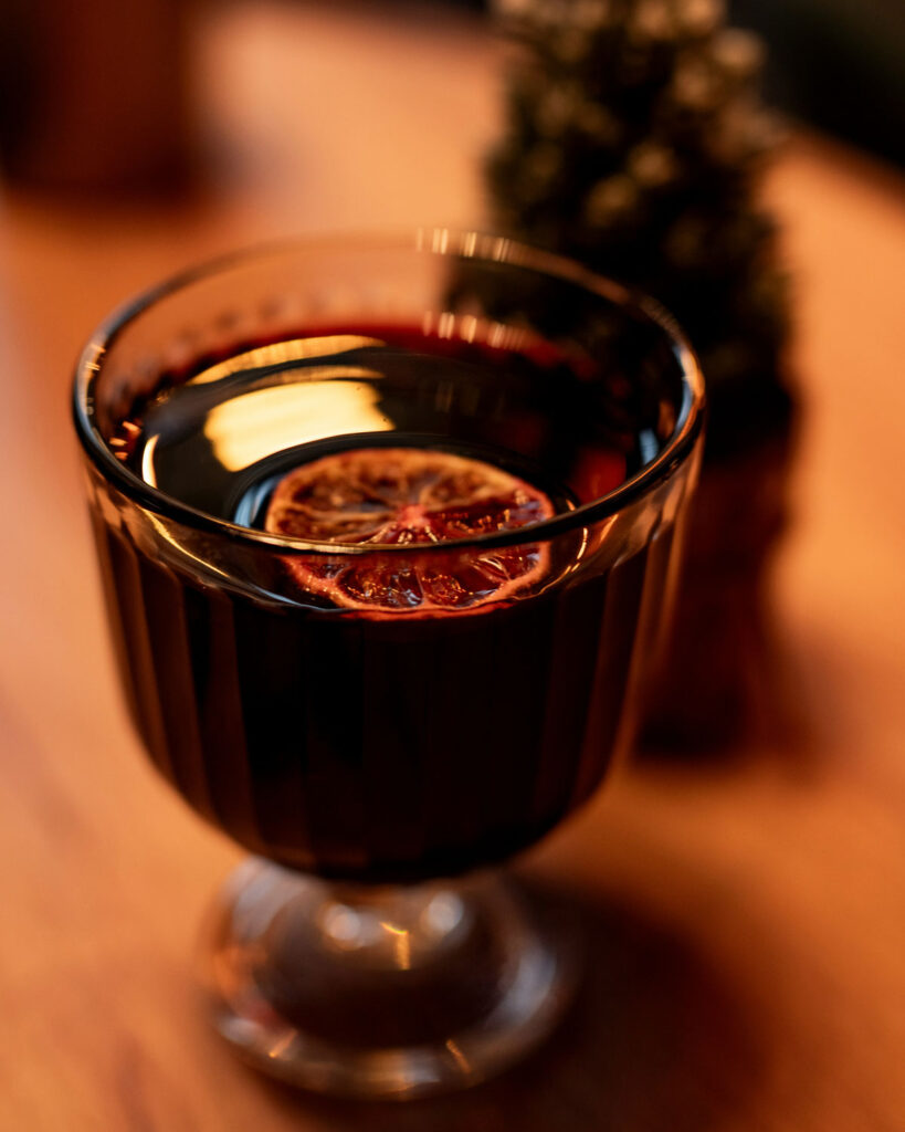 Edles Glas Vin Brulé mit getrockneter Orangenscheibe auf Holzuntergrund im warmen Licht