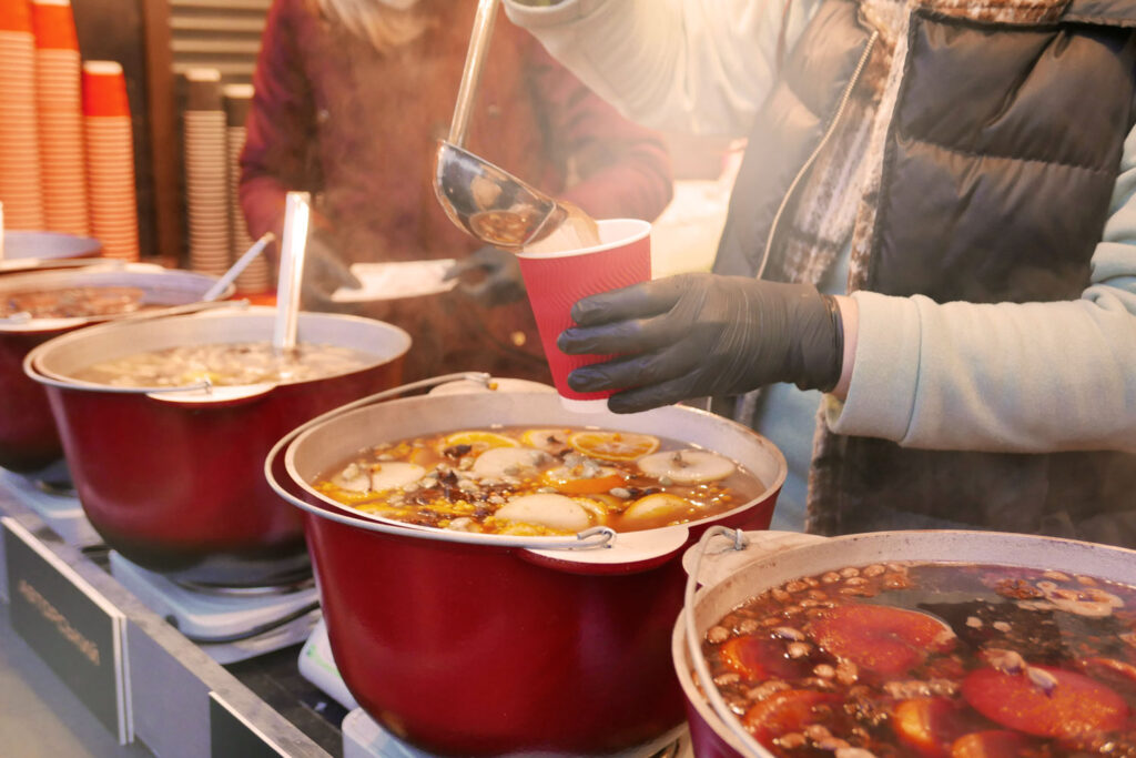 Verkauf von Vin Brulé auf italienischem Markt mit mehreren dampfenden Töpfen voller Gewürze und Zitrusfrüchte