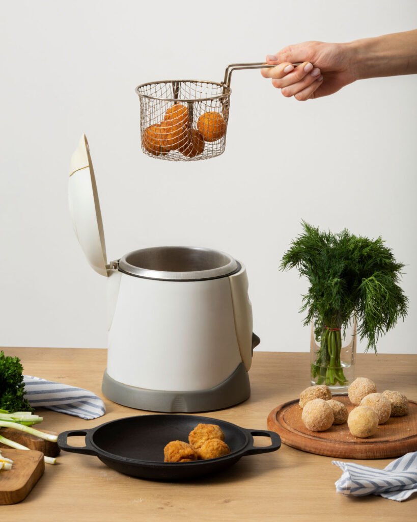 Frittierkorb mit panierten Bällchen wird in eine weiße Heißluftfritteuse gesenkt, auf dem Tisch liegen Kräuter und Zutaten bereit