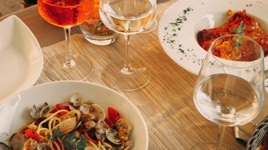 Typisches italienisches Mittagessen mit Spaghetti alle Vongole, Lasagne, Aperol Spritz und Weißwein – mediterrane Lebensfreude als immaterielles Kulturerbe