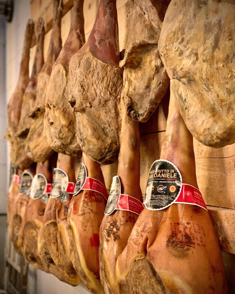 Mehrere ganze Schinken von Prosciutto di San Daniele DOP hängen in der Reifekammer – traditionell gereifter italienischer Rohschinken.
