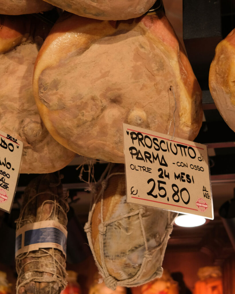 Prosciutto di Parma DOP mit Preisschild in einer italienischen Salumeria – über 24 Monate gereifter Rohschinken am Knochen.