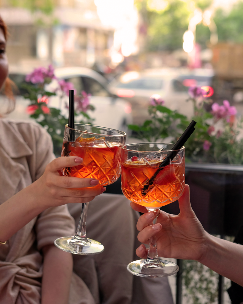 Freunde stoßen mit Aperol Spritz an – klassischer Aperitivo in Italien auf einer sommerlichen Café-Terrasse.