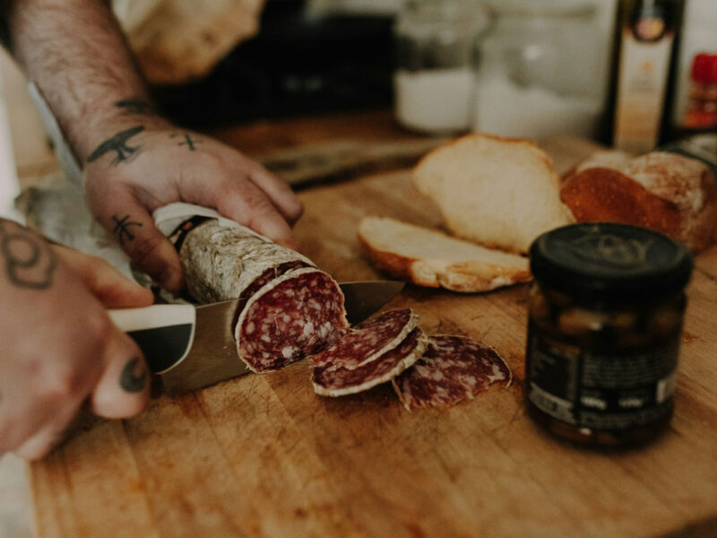 Handwerkliche Herstellung von Salame – italienische Rohwurst wird frisch geschnitten und mit Brot serviert