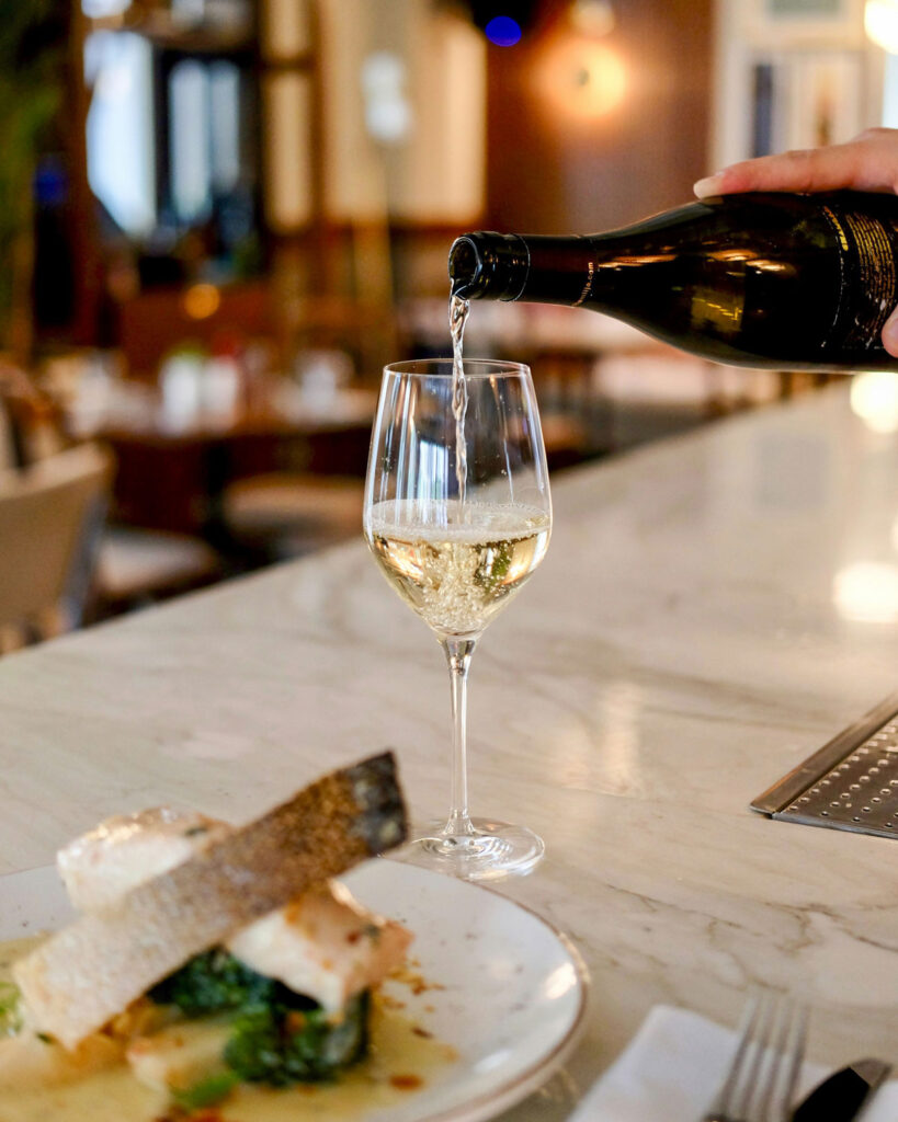Weißwein wird ins Glas eingeschenkt im Restaurant – servierter Weißburgunder als eleganter Begleiter zu feiner Küche.