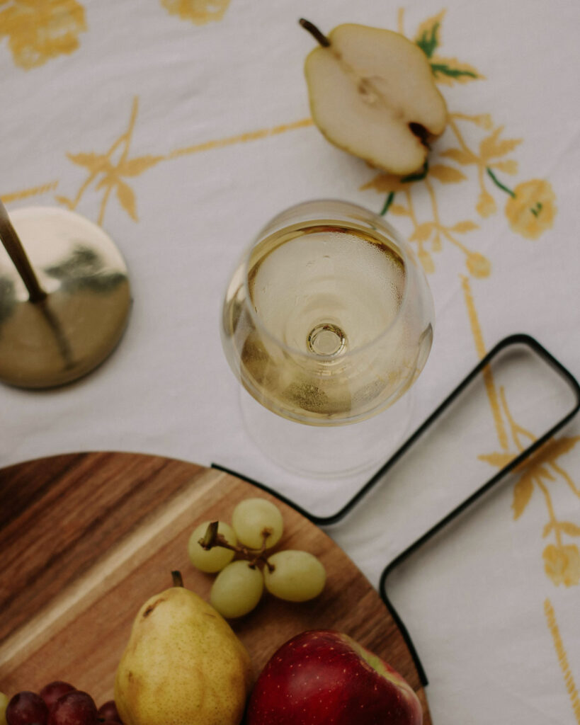 Glas Weißwein mit Trauben und Obst auf Tisch – typische Aromen und Genussmomente von Weißburgunder (Pinot Bianco).