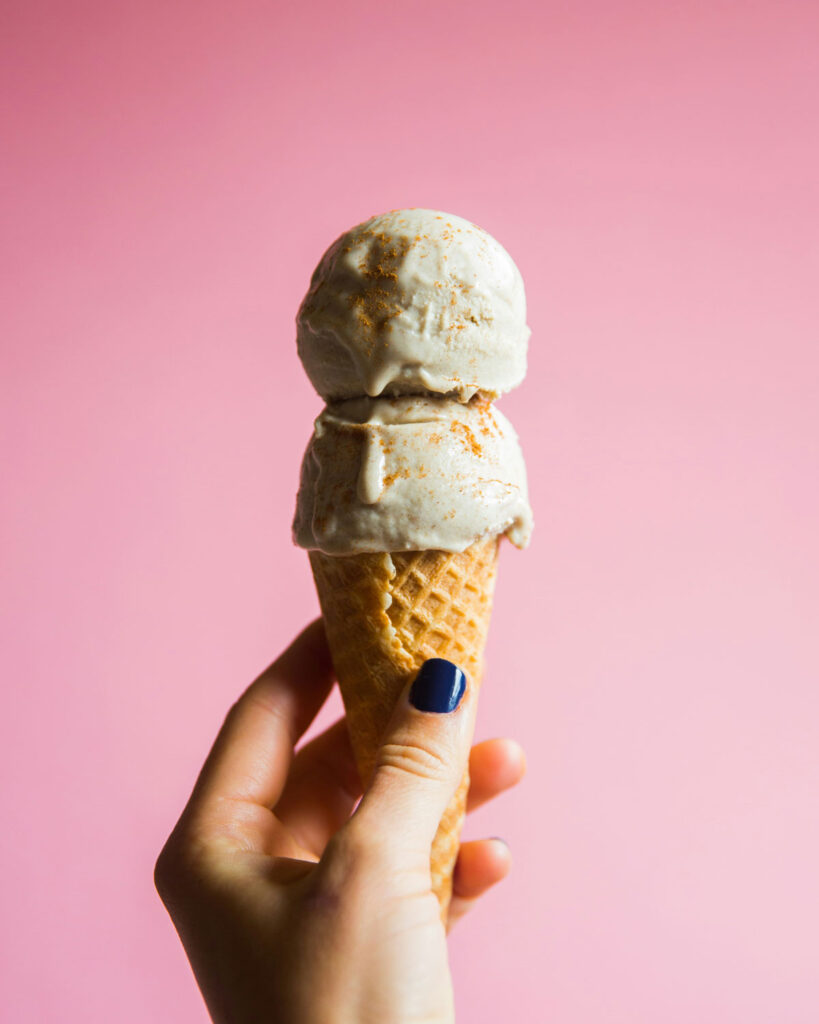 Italienisches Gelato in der Waffel – zwei Kugeln cremiges Speiseeis vor rosa Hintergrund